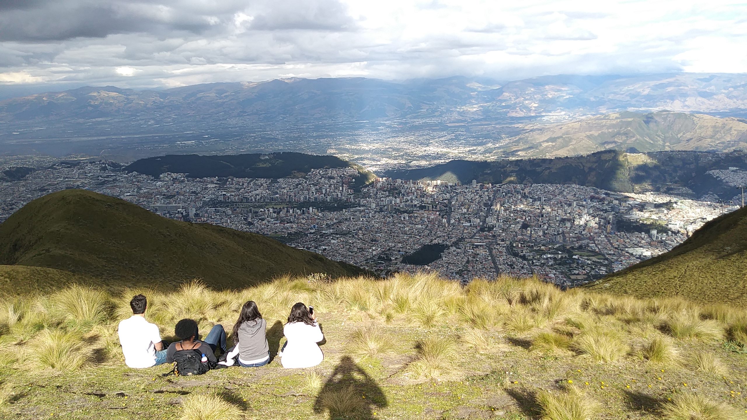 Four students sitting on a grassy hill overlooking a sprawling city in Spain