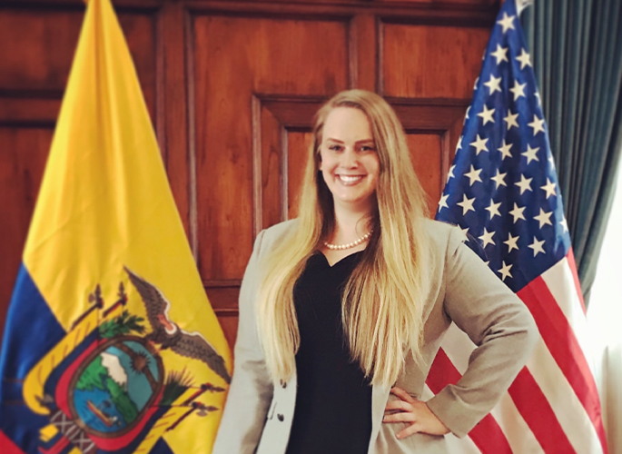 Amanda Tollefson smiling next to the American and Ecuadorian flags