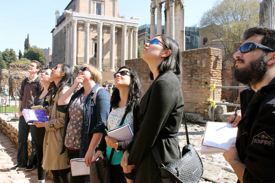 Group of students starting at unseen architecture, with Greek temple architecture in the background