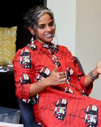 Professor Anu Taranath seated and smiling while wearing a bright red patterned dress