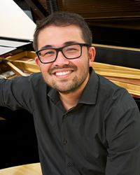 Nicholas Tagab smiling to camera, while leaning against a piano