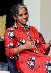 Professor Anu Taranath seated and smiling while wearing a bright red patterned dress